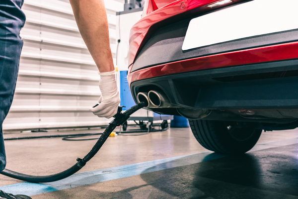 A mechanic in gloves prepares to service the exhaust of a red car in a workshop, focusing on maintenance tasks.