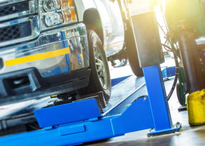 A silver pickup truck is raised on a blue hydraulic lift in a garage, with sunlight highlighting the equipment.